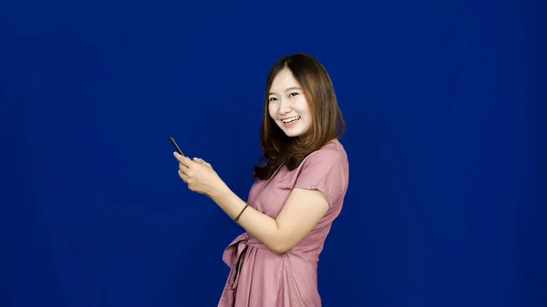 Красива Азіатська Жінка Посміхається Дивитися Телефон Ізольований Синій Фон — стокове фото