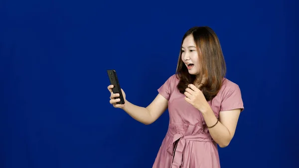 アジア系女性の驚きの表情は携帯電話の青の背景を見る — ストック写真