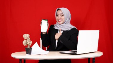 İş yerindeki Asyalı kadın yeşil ekran cep telefonuyla tesettüre girmiş, kırmızı arka plan izole edilmiş.