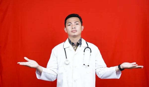 孤立した赤い背景の上に立って聴診器を身に着けているアジアの医師の男は 腕や手を上げと混乱表現 疑いの概念 — ストック写真