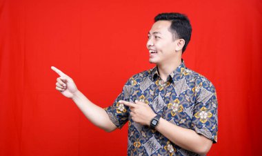 Batik giyen Asyalı bir adam boş alanı işaret ederek izole edilmiş kırmızı arka plan