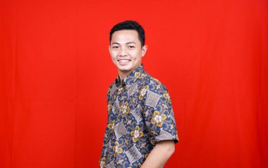 Stüdyoda kırmızı arkaplan ile izole edilmiş Batik elbiseli Asyalı adam stili