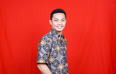 Stüdyoda kırmızı arkaplan ile izole edilmiş Batik elbiseli Asyalı adam stili