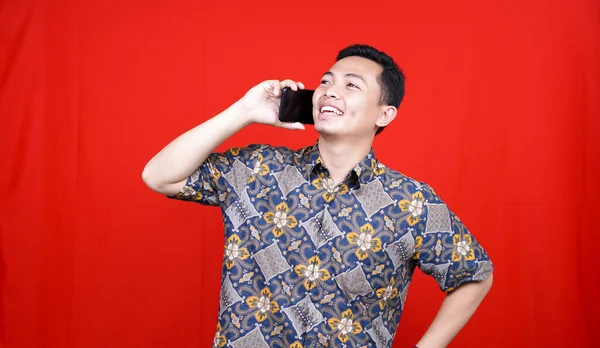 Azji Człowiek Wzywa Szczęśliwy Ekspresja Batik Ubrania Izolowane Czerwone Tło — Zdjęcie stockowe