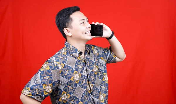 Azji Człowiek Wzywa Szczęśliwy Ekspresja Batik Ubrania Izolowane Czerwone Tło — Zdjęcie stockowe