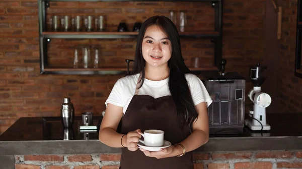 アジアの女性バリスタ笑顔とコーヒーショップカウンターでカメラを探しています バリスタ女性がカフェでコーヒーカップを保持 — ストック写真