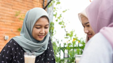 Kafede arkadaşlarıyla gülen Asyalı grup tesettürcüsü kadın.