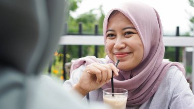 Kafede arkadaşlarıyla sırıtan Asyalı tesettür kadın grubu.