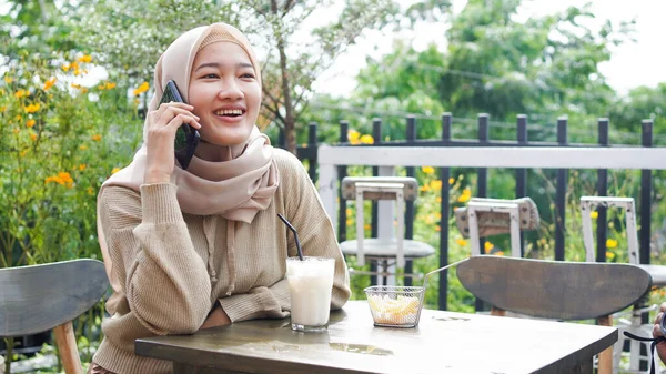 happy Asia hijab woman using smart phone and calling, sitting at cafe