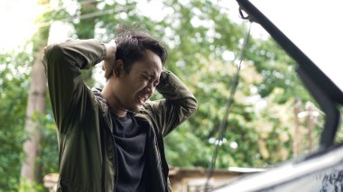 Asyalı adam kafası karışıkken arabanın kaputunu açtı.