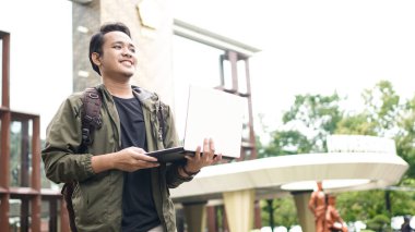 Sırt çantalı, dizüstü bilgisayarlı gülümseyen Asyalı adam.