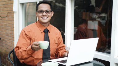 Girişimciler bilgisayarda çalışıyor, kahve içiyor ve gülümsüyor.