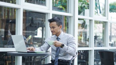 Girişimciler bilgisayarda çalışıyor, kahve içiyor ve gülümsüyor.