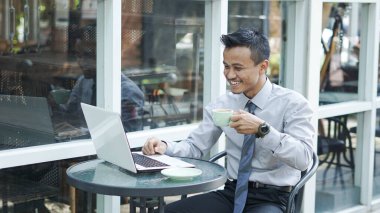 Girişimciler bilgisayarda çalışıyor, kahve içiyor ve gülümsüyor.