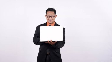 Takım elbiseli bir iş adamı dizüstü bilgisayar tutuyor ve beyaz arka planda izole edilmiş kameraya bakıyor.