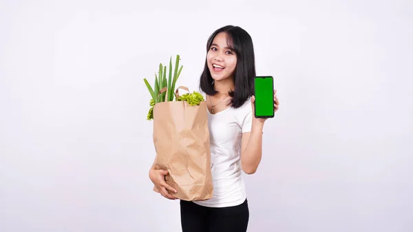 亚洲女人 拿着纸袋新鲜蔬菜 拿着绿色荧幕电话 背景是孤立的白色 — 图库照片#