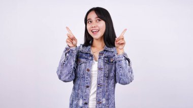 Kot ceket giymiş, gülümseyen Asyalı bir kadın ve izole edilmiş beyaz bir arka planı olan elleri işaret ediyor.