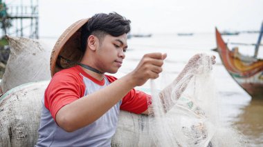 Genç bir balıkçının portresi sahilde bir balık ağı hazırlıyor.