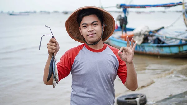 Šťastný Mladý Rybář Pláži Drží Své Úlovek Ryby Ukazuje Před — Stock fotografie