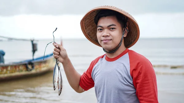 快乐的年轻渔夫在海滩上拿着他的渔获物 在他的船前面出现 — 图库照片#