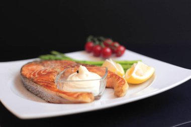 Sebze ve baharatlı somon bifteği: kuşkonmaz, domates, zencefil, biber, tuz, kırmızı biber, soğan, limon ve siyah zemin üzerinde zeytin yağı. Sağlıklı beslenme konsepti. Üst görünüm.