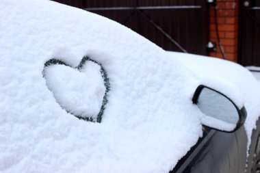 Arabanın ön camına çizilmiş bir kalp. Taze Noel karıyla kaplı..