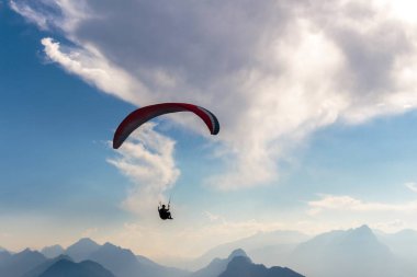 Solo paraglider silueti dramatik mavi gökyüzüne ve aşağıdaki sisli dağlık dağlara doğru yükseliyor..