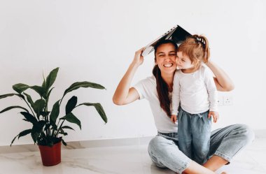 Mutlu anne-kız çatıyı yapıyor. Kadın dizüstü bilgisayarı başının üstünde tutuyor. Sosyal mesafeyi korumak ve evden çalışmak.