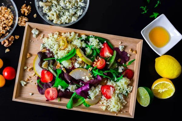 Salad of couscous with fresh cherry tomatoes, strawberries, lettuce, lemon and honey, blues cheese and walnuts on wooden tray