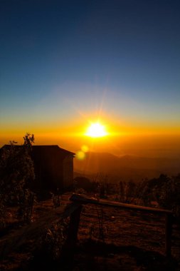 Una hermosa cabaa en la montaa con un amanecer de fondo en colores amarillos y naranjas