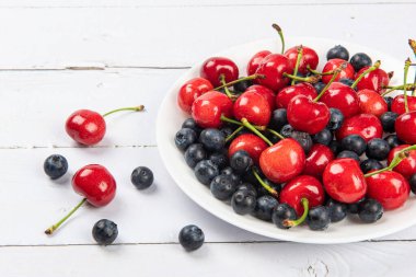 Taze organik meyve kirazı ve ahşap zemin üzerinde yabanmersini.