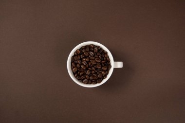 Kahverengi arka planda kahve çekirdekleri olan bir fincan kahve.