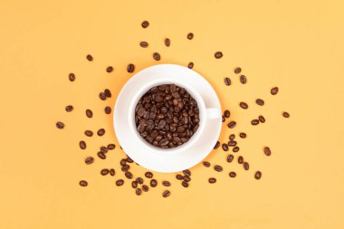 Kahve fincanı ve kahve çekirdekleri sarı arka planda.