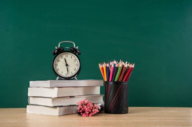 Karatahta arkaplan kopyalama alanı altında kalemle birlikte ders kitabı yığınındaki alarm saati