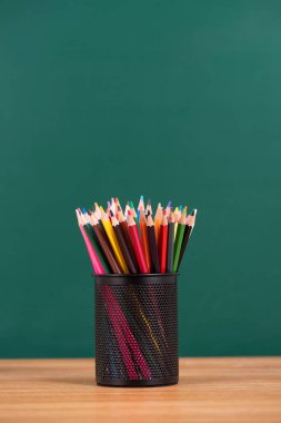 Masanın üzerinde yeşil karatahta arka planında kurşun kalem olan metal bardak.