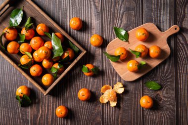 Siyah ahşap masada yeşil yapraklı taze mandalinalar, yakın plan.