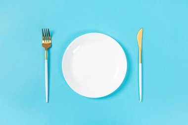 Mavi arkaplandaki çatal bıçak takımlı boş tabak