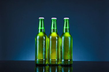 Mavi arka planda damlaları olan yeşil bira şişesi