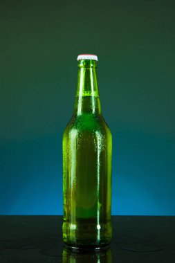 Mavi arka planda damlaları olan yeşil bira şişesi