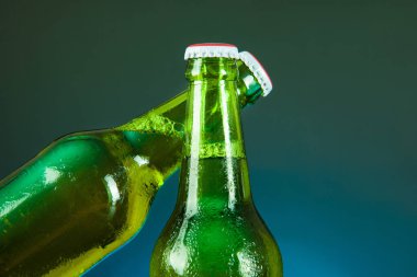 Yeşil bira şişesi mavi arka planda damlalar ile tezahürat yapar