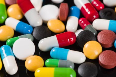 Siyah arka planda çeşitli ilaç hapları, haplar ve kapsüller.