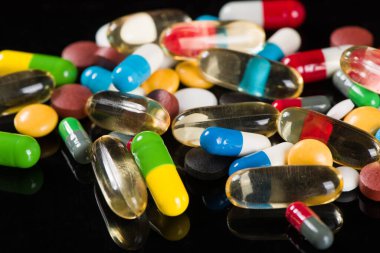 Siyah arka planda çeşitli ilaç hapları, haplar ve kapsüller.