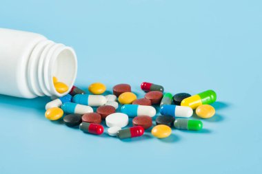 Mavi arka planda çeşitli ilaç hapları, haplar ve kapsüller.