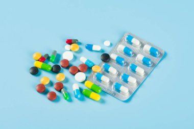 Mavi arka planda çeşitli ilaç hapları, haplar ve kapsüller.