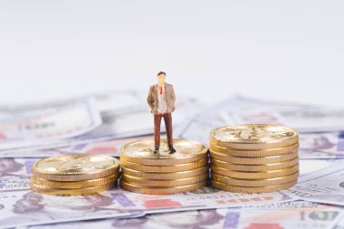 miniature businessman stand  on  gold coins on US dollar banknote background
