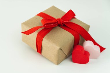 Kırmızı kurdeleli hediye kutusuna yakın plan ve beyaz arka planda iki kalp..