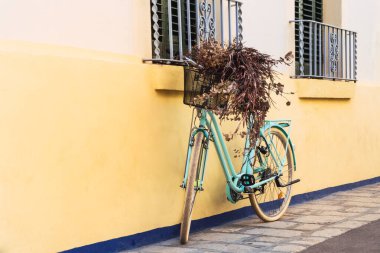 Turkuaz mavi bisiklet Sitges, Barcelona 'da sarı bir duvara yaslanıyor.