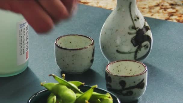 Judías de soja con sal y sake botella y tazas — Vídeo de stock