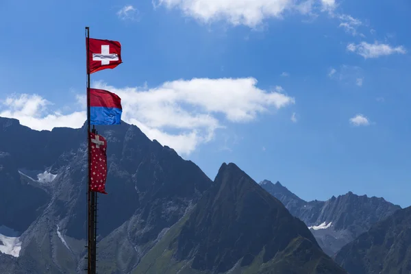 Beautiful switzerland flag with mountain background on summer period on. a pole in mountains — Stock Photo, Image