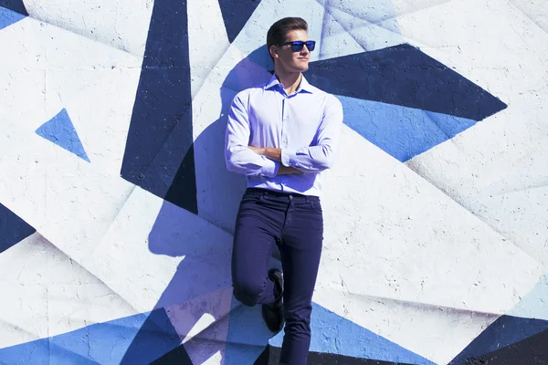 Giovane uomo d'affari bello in abito blu e occhiali guardando contro parete dipinta . — Foto Stock